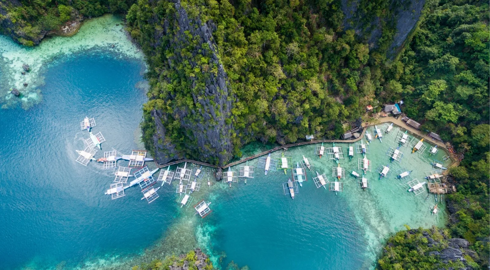Aerial view of traditional Filipino bangka boats moored beside towering limestone cliffs in Bacuit Bay