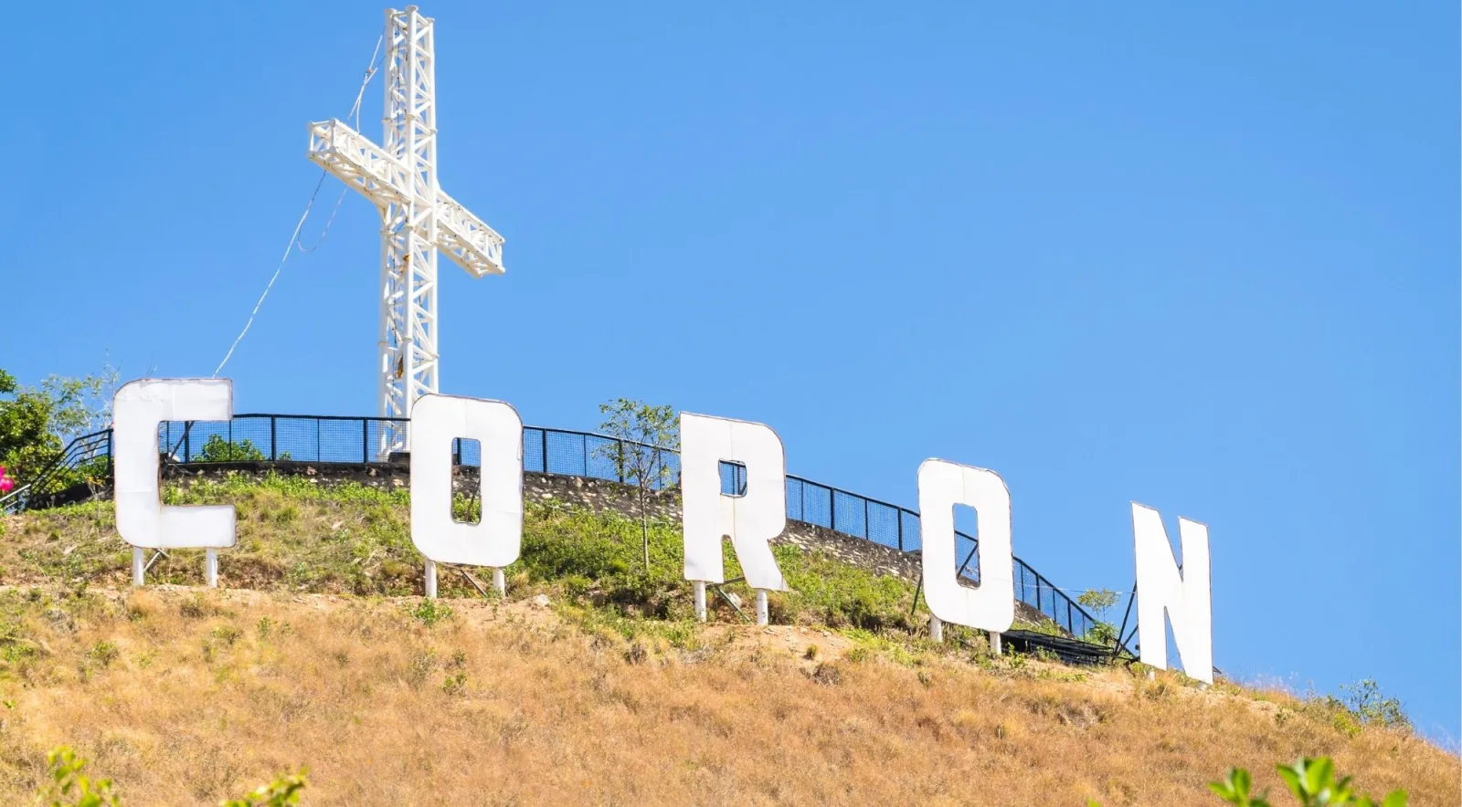 The CORON letters and cross on a hilltop against a bright blue sky in Coron Town, Palawan
